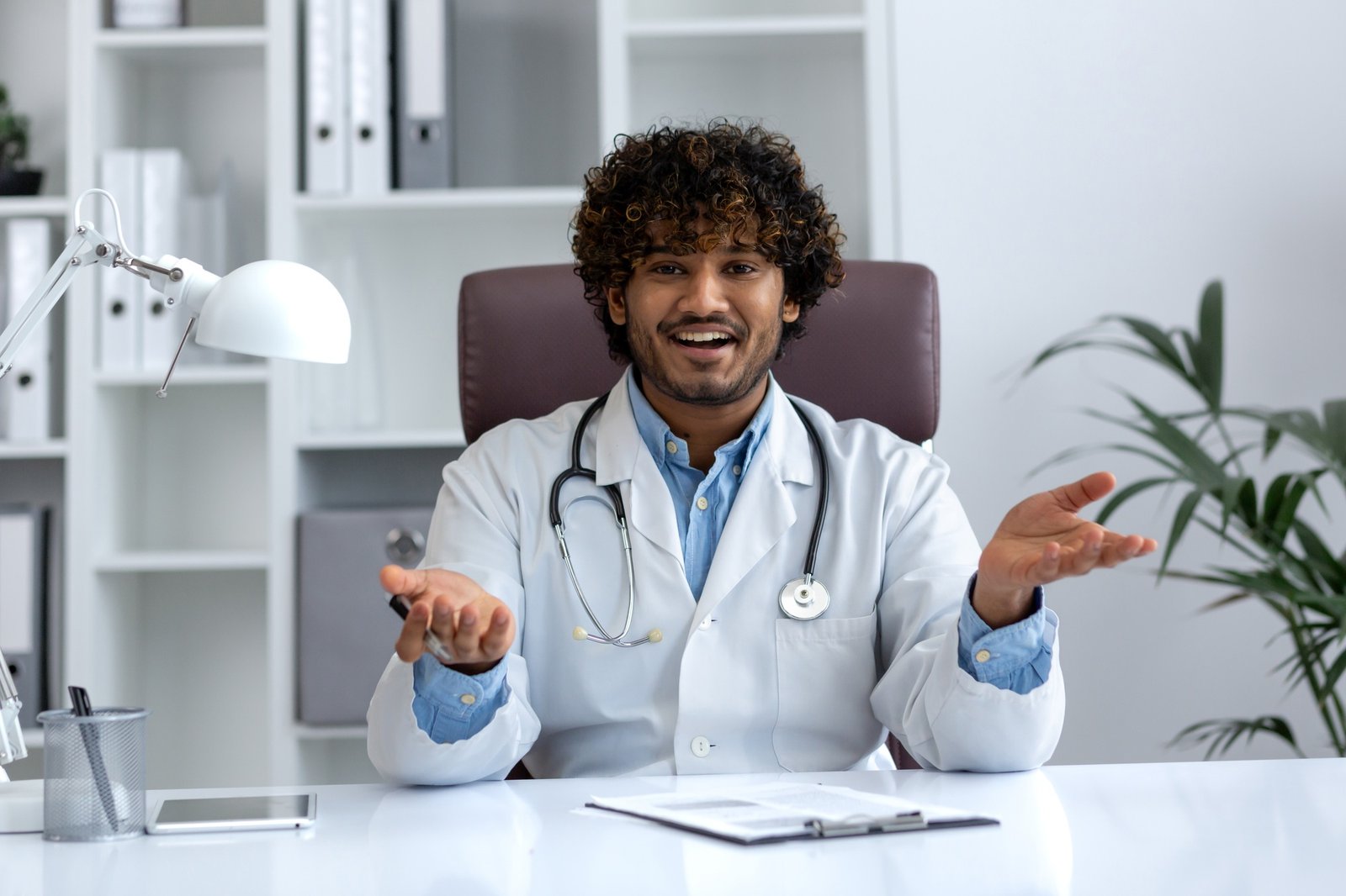 Friendly young doctor with a stethoscope in a well-lit medical office welcoming patients
